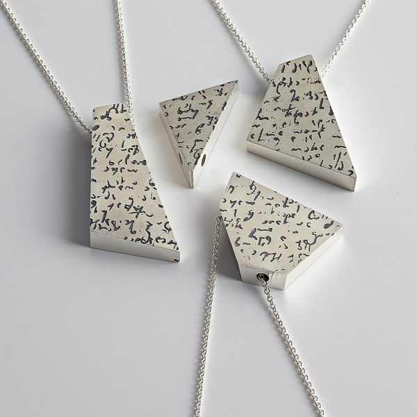 Four angular silver pendants that fit together like a puzzle. All pendants have etched and oxidised handwriting