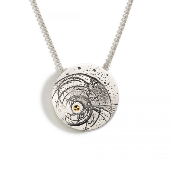 Circular silver statement pendant with an image of a black hole etched and oxidised onto the surface and a disc of 18ct gold in the centre of the black hole